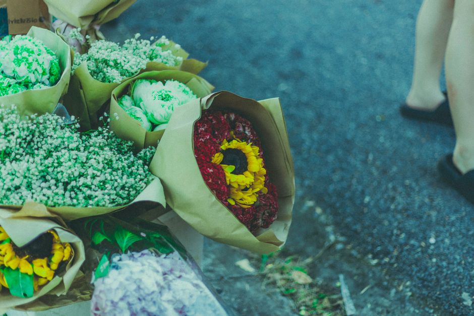 A collection of flower bouquets arranged on the ground, featuring a variety of fresh flowers including red and yellow chrysanthemums, white baby's breath, and green foliage, all wrapped in beige paper
